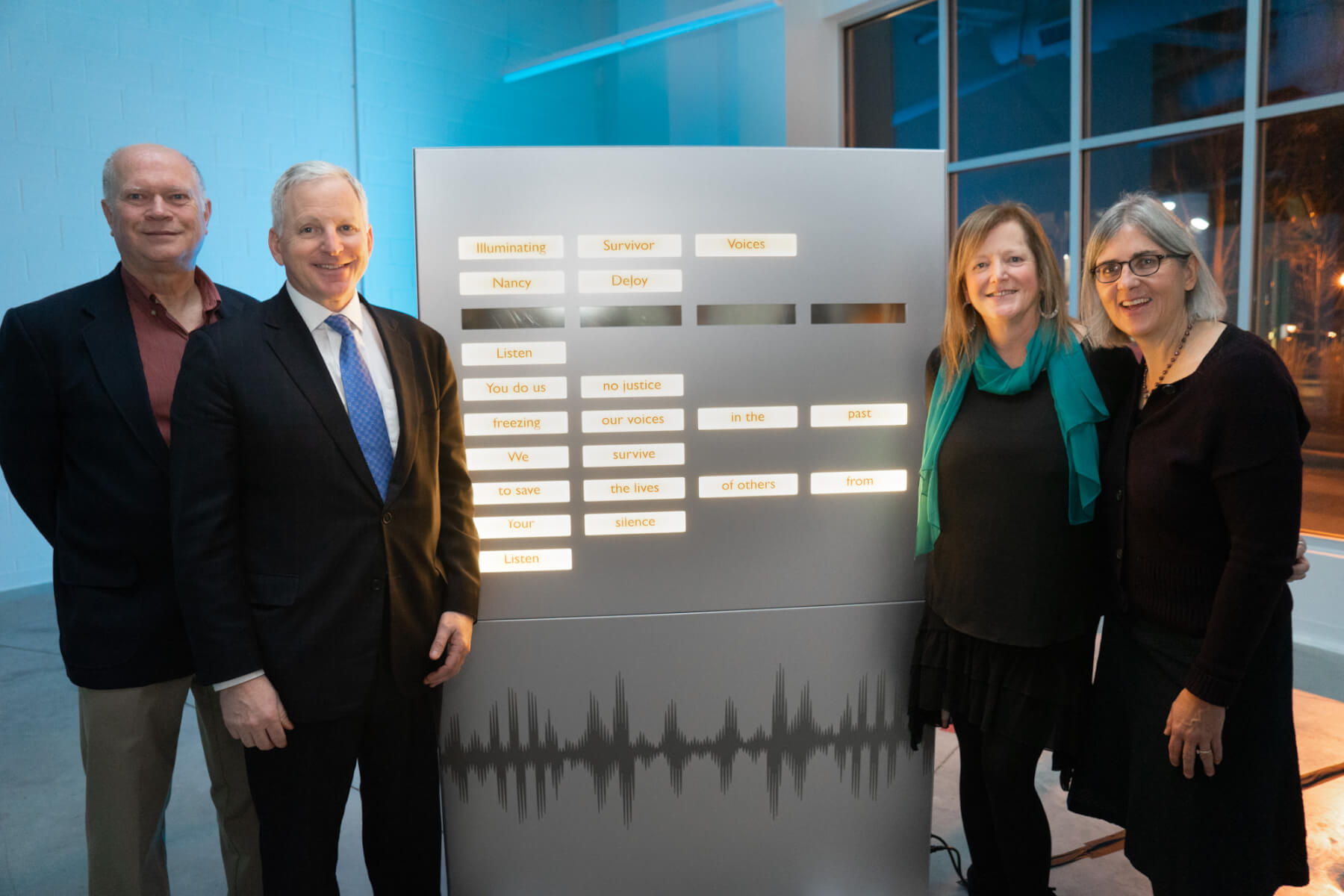 Jeff Jackson, Dave DeJoy, Nancy DeJoy and Giana Phelan standing next to the poem Illuminating Survivor Voices